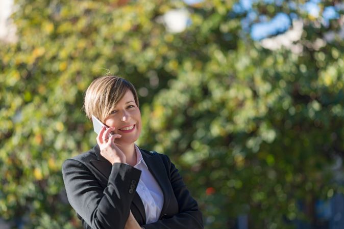 Happy businesswoman speaking on phone in front of hedge