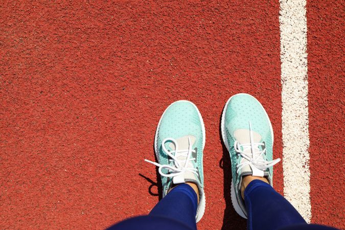 Female legs in sneakers on red athletic track background, space for text