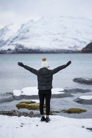 Anonymous person on pond shore against highland in winter