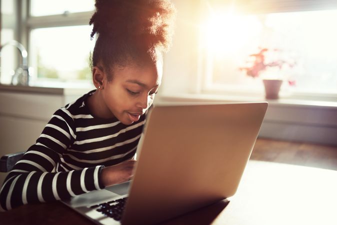 Girl works on laptop in sunny kitchen