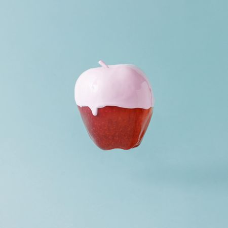 Red apple with pink syrup on pastel blue background