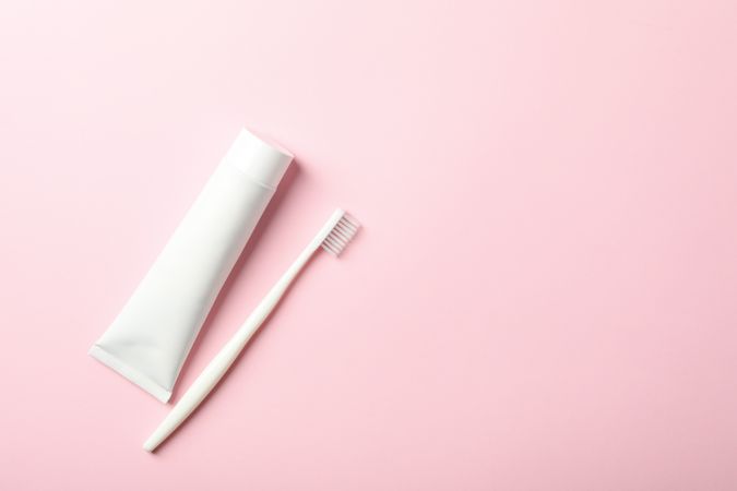 Toothbrush and toothpaste on pink background, space for text