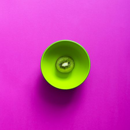 Kiwi in green bowl on purple background