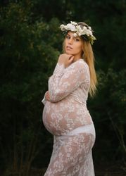 Pregnant woman with closed eyes in white lace dress touching chin while standing in forest
