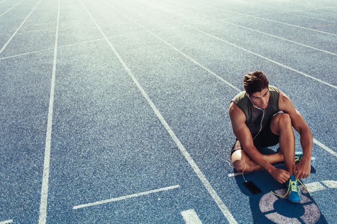 Sprinter tying shoe lace sitting on running track with copy space