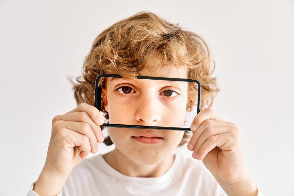 Child posing with his mobile phone and photos made of parts of his face