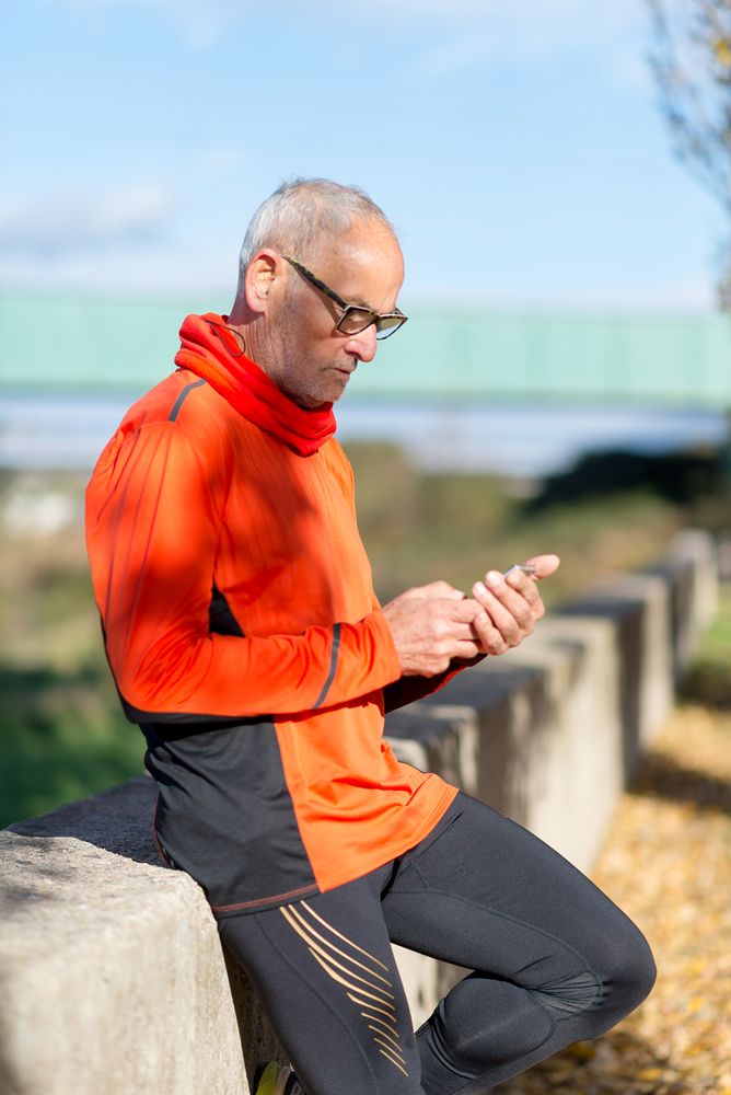 Grey haired male looking down at smartphone in park