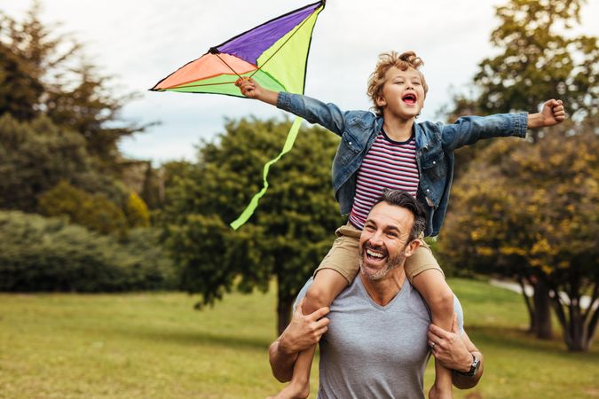 Little son with his father playing in a park with a kite