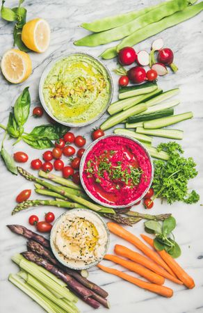 Flat-lay of fresh colorful vegetables and dips with hummus, avocados, asparagus, carrots
