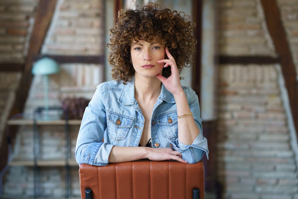 Serious young woman wearing denim jacket sitting on leather chair