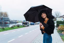 Smiling Black woman with umbrella on street