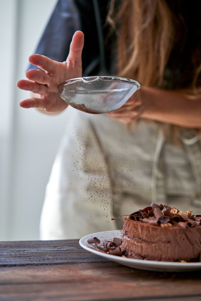 Woman sprinkling cocoa powder on cake