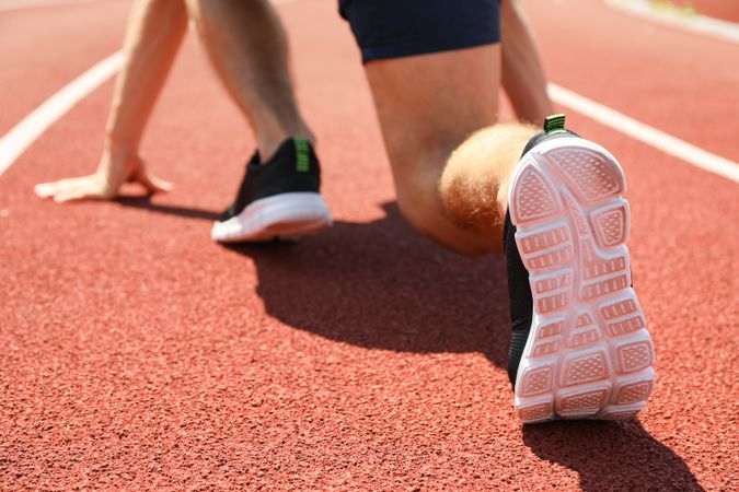 Sportsman low starting to run on red athletic track, close up