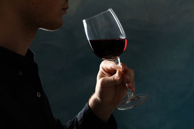 Young man holding red wine glass against dark background, space for text