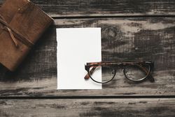Leather-bound notebook, piece of paper and spectacles on wooden table