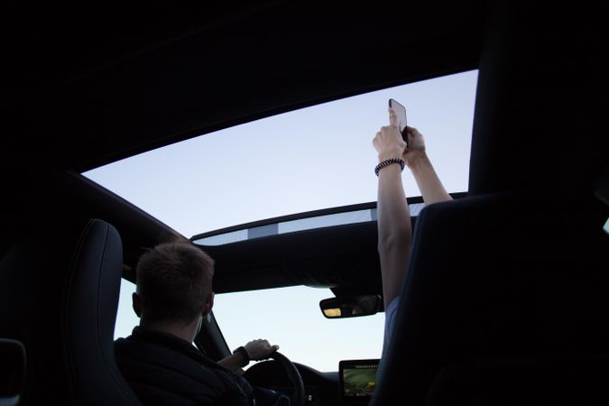 Two people having fun on a road trip taking photos out the sunroof