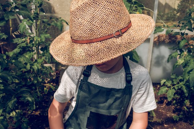 Preteen boy sitting in garden bed in straw hat