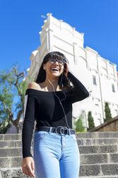 Young happy woman wearing earphones spending free time outdoors in the sun