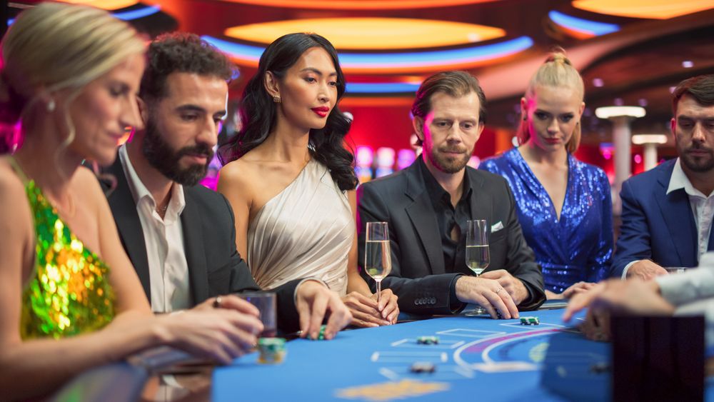 Group of Casino Goers Enjoying Time in a Modern Casino, Friends Placing Blackjack Bets, Professional Female Croupier Deals Cards.