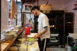 Pizza man adding zucchini to pizza