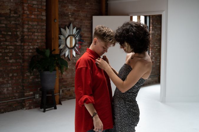 Young woman adjusts the collar of her partner’s red shirt