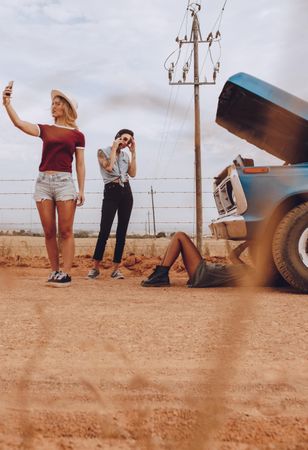 Female friends making phone calls at side of quiet road after their car broke down