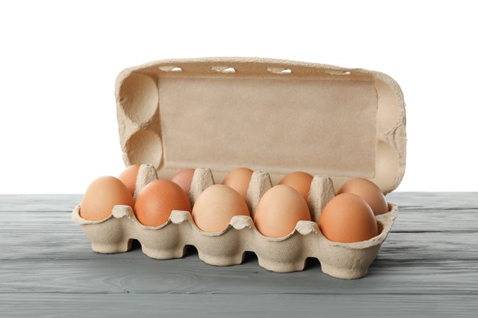 Few raw chicken eggs in carton box on wooden table against light background