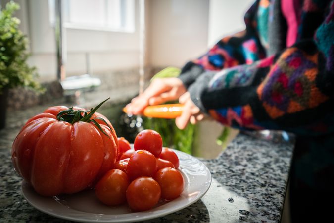 Crop woman washing tomato over sink