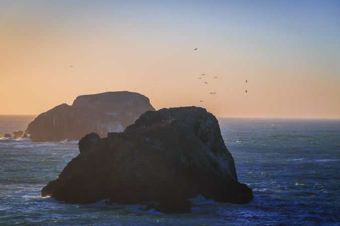 Two large rocks in the Pacific Ocean with birds flying around