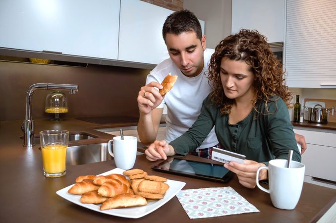 Couple eating breakfast while buying something on tablet