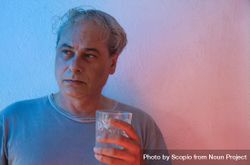 Portrait of serious middle aged man in gray shirt holding a glass of water against light background in UV lit studio 0WLoP5