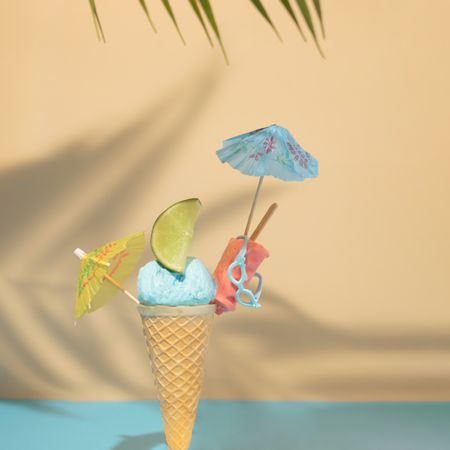Blue ice cream in cone with several cocktail parasol and sunglasses on beach background