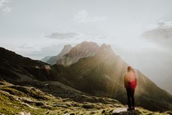 Man with backpack standing on rocky hill looking at mountains