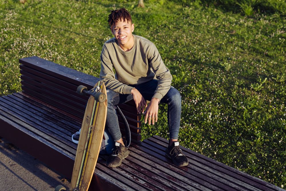Young Black man sitting on bench with skateboard