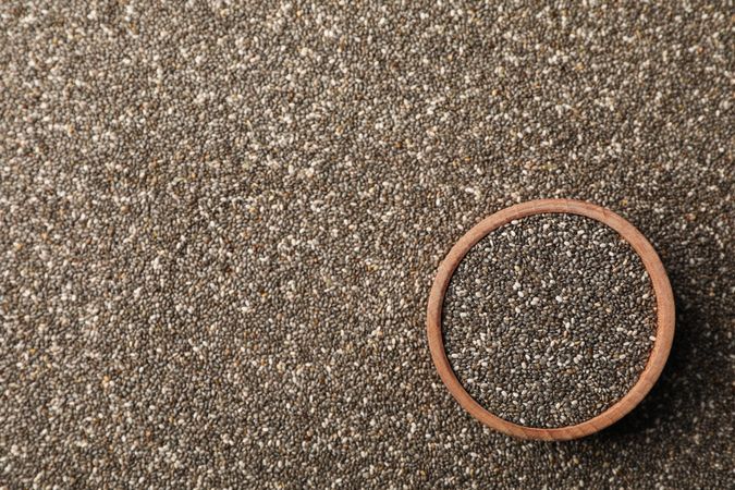 Wooden bowl and chia seeds on whole background, space for text