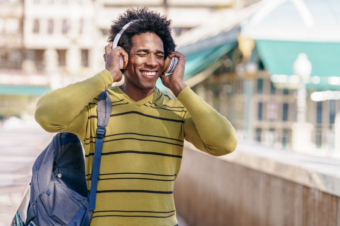 Man smiling in yellow shirt listening to music walking outside