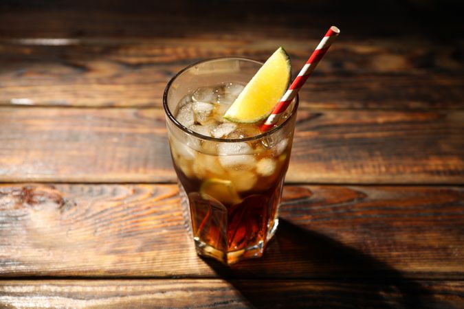 Glass with ice cola and lime slice on wooden background