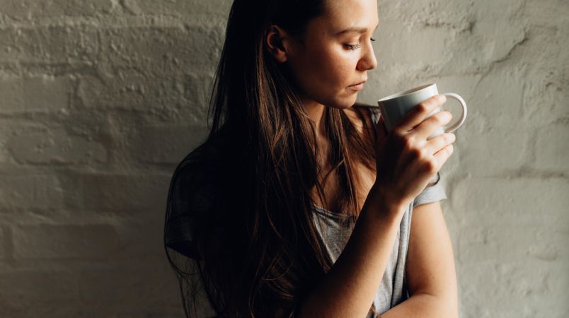 Close up of a woman standing against a wall holding a cup of coffee