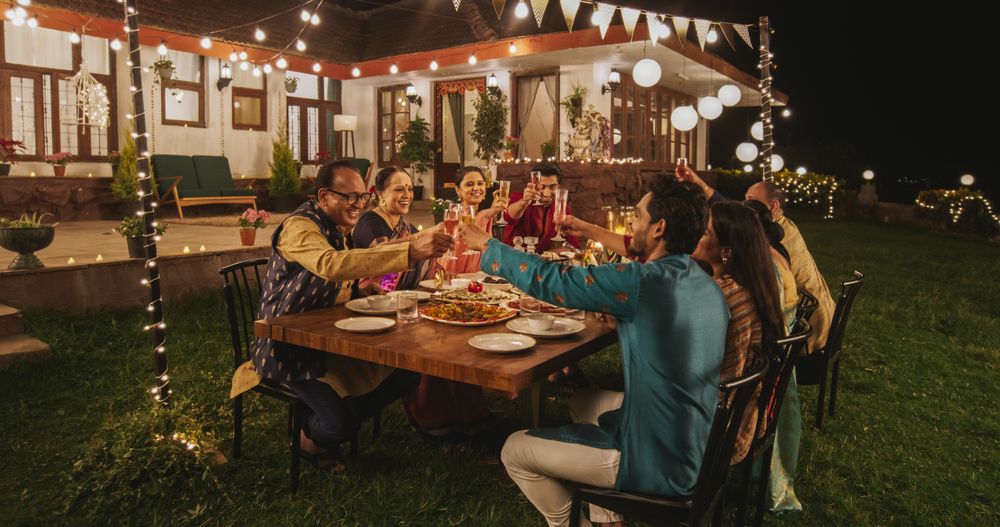 Big Indian Family Celebrating Diwali: Family Gathered Together on a Dinner Table in a Backyard Garden Full of Lights.