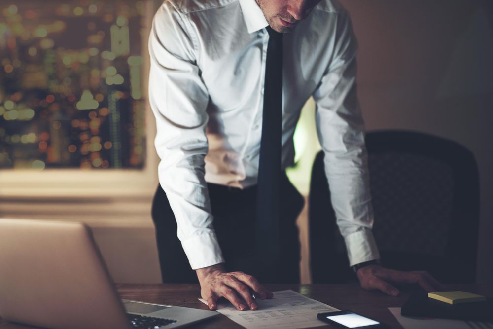 Focused man standing over documents and laptop