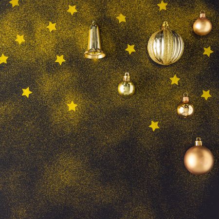 Golden Christmas decorations of stars, glitter bells and baubles on dark background