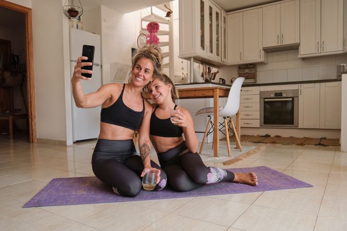 Woman taking selfie with girl on smartphone at home