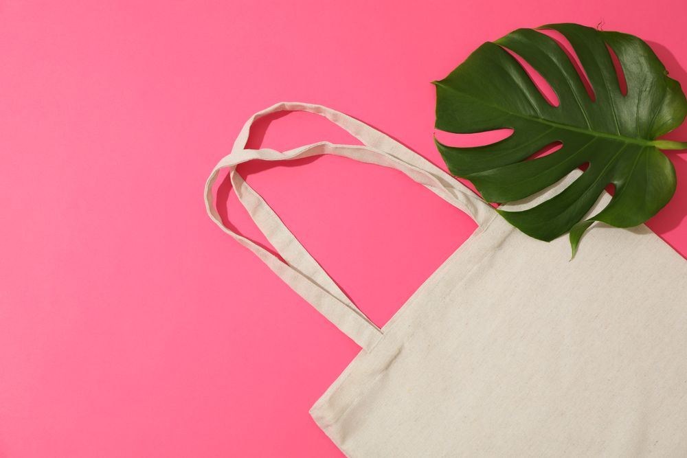 Eco bag and palm leaves on color background, top view