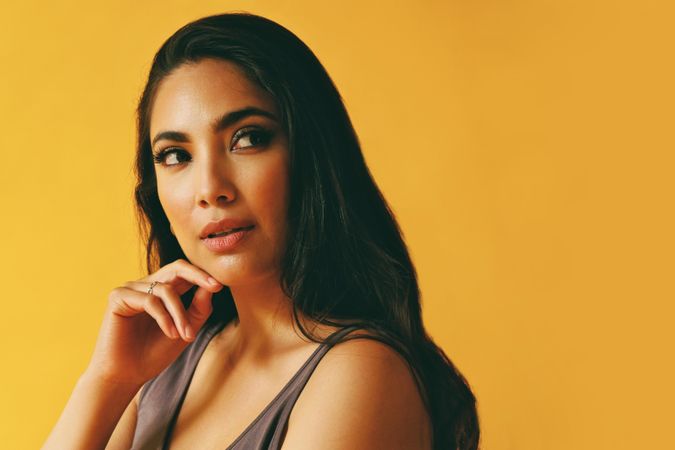 Wistful Hispanic woman looking away from camera in yellow room, copy space