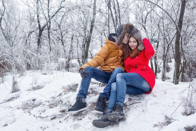 Teenage boy kissing girlfriend sitting in snowy forest
