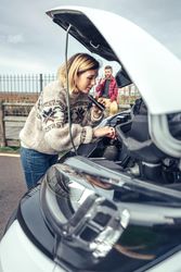 Female in woolen sweater working on car engine, vertical