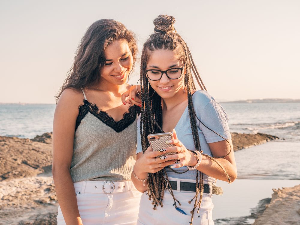 Smiling trendy young women using smartphone on beach