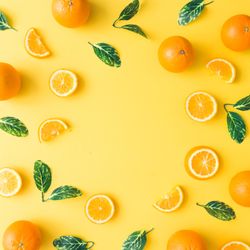Oranges and green leaves on pastel yellow background