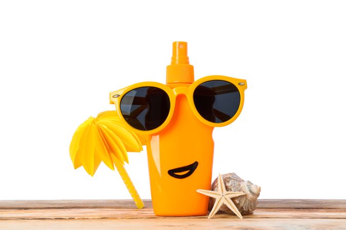 Sunscreen spray with sunglasses, starfish, seashell and decorative palm on wooden table, isolated on plain background. Safe tan