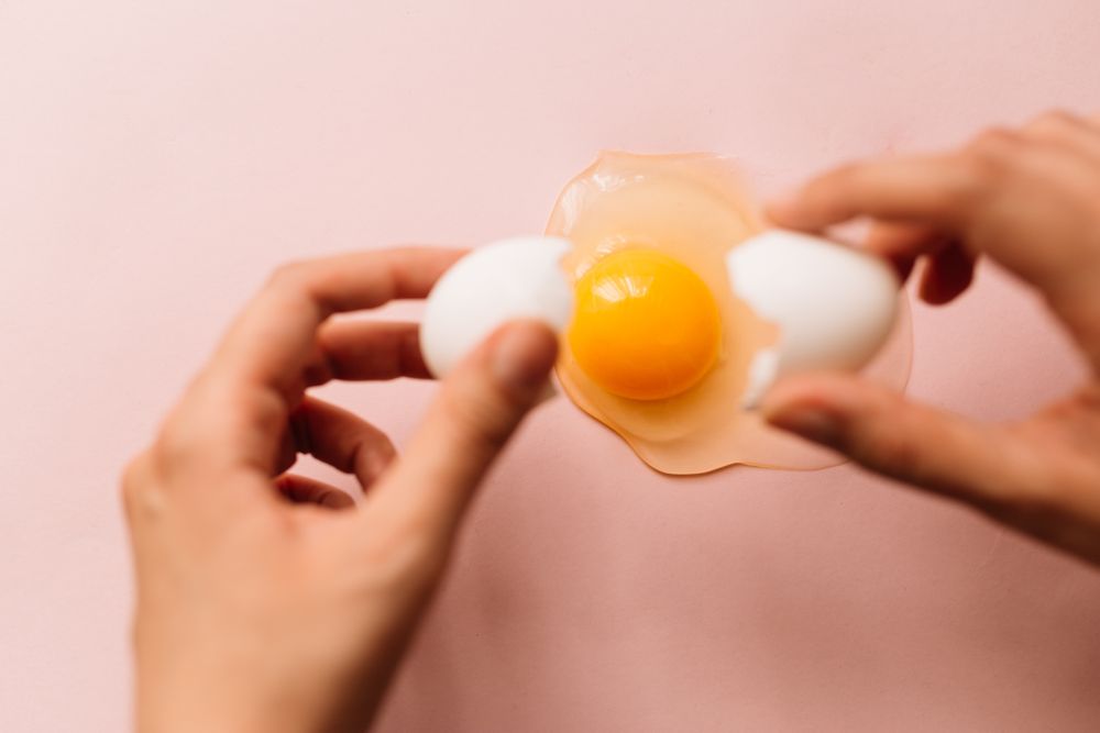 Unrecognizable person breaking chicken egg on table